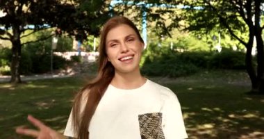 Güzel genç bir kadının portresi Zafer jesti gösteriyor ve parkta kameraya gülümsüyor.   