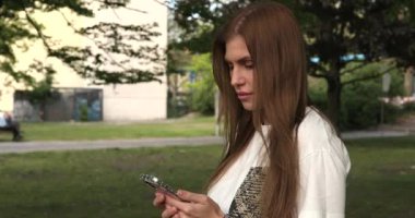 Akıllı telefon kullanan ve parkta zaferi kutlayan güzel bir genç kadının portresi.