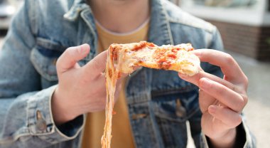 Sokakta bir dilim pizza yiyen genç adamın yakın çekim görüntüsü..        
