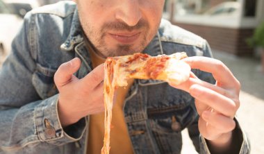 Yakışıklı genç adam sokakta pizza yiyor..       
