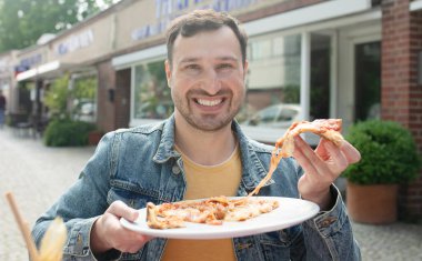 Yakışıklı genç adam sokakta pizza yiyor..       