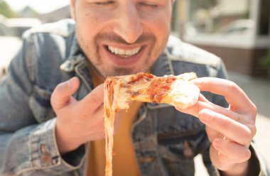Yakışıklı genç adam sokakta pizza yiyor..       