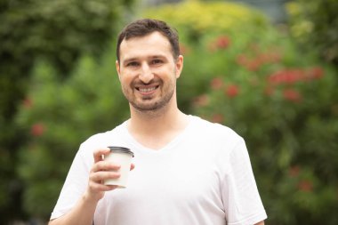 Yakışıklı genç adam sokakta kahve içiyor.