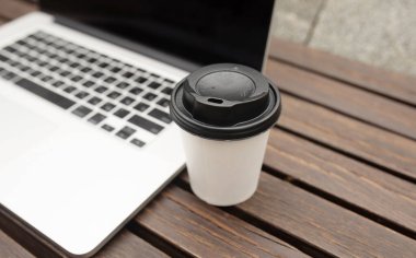 Kahve dükkanında çalışma alanındaki ahşap masada bir fincan kahve ve dizüstü bilgisayar. Çevrimiçi iş, kafeden çalışmak, taşınabilir ofis konsepti, kapat 