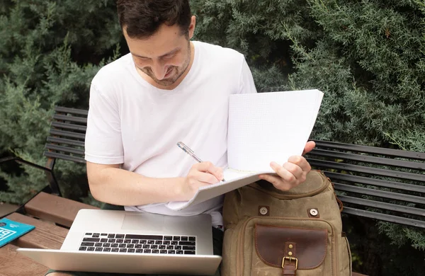 Joven Sonriente Sentado Banco Usando Ordenador Portátil Escritura Cuaderno Parque — Foto de Stock