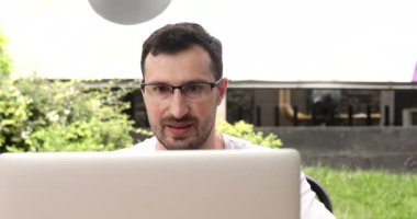 Gözlüklü yakışıklı sakallı genç bilgisayarını kapatıp dışarıda kahve içiyor.