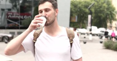 Yakışıklı genç adam sokakta kahve içiyor.
