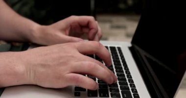 Dışarıda dizüstü bilgisayarda daktilo kullanan genç adamın yakın görüntüsü.