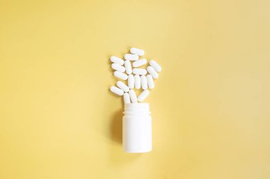 Sarı arka planda beyaz ilaç hapları.