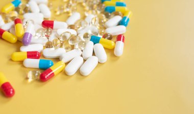 Sarı arka planda renkli haplar ve kapsüller, tıbbi geçmiş 