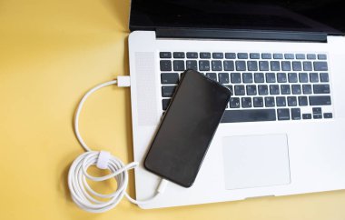sarı arkaplanda şarj olmak için güç kablosu olan bilgisayar ve akıllı telefon.