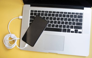 sarı arkaplanda şarj olmak için güç kablosu olan bilgisayar ve akıllı telefon.