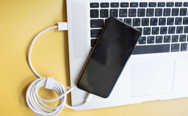 sarı arkaplanda şarj olmak için güç kablosu olan bilgisayar ve akıllı telefon.