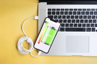 Cep telefonu bataryasını dizüstü bilgisayarla şarj ediyor, akıllı telefonu sarı arka planda..