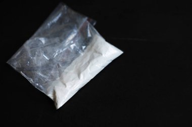 Beyaz plastik uyuşturucu torbası, siyah zemin üzerinde beyaz toz olan çanta.   
