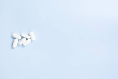 Mavi arka planda ilaç haplarının üst görüntüsü. Mavi masaya dağılmış beyaz haplar..