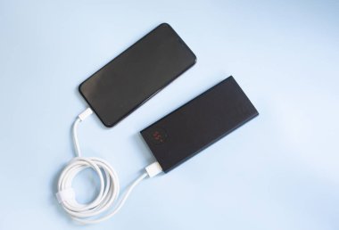 Mavi arka planda siyah güç bankasıyla şarj olan bir akıllı telefon. Kopyalama alanı ile yakın plan görünüm.