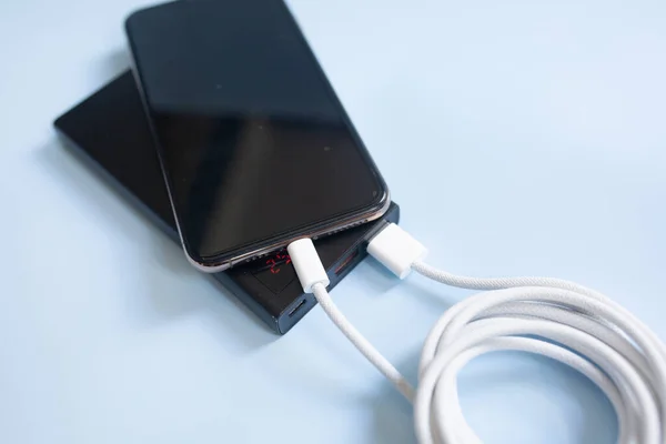 ブラックパワーバンクをブルーバックに充電したスマートフォン コピースペースでクローズアップビュー — ストック写真