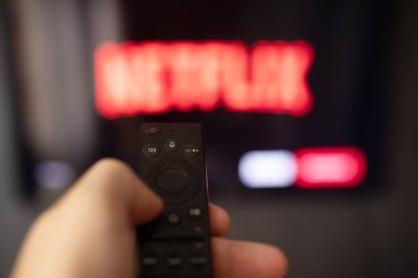 Adamın elinde arka planda televizyon ekranı olan akıllı bir televizyonun uzaktan kumandası var. 