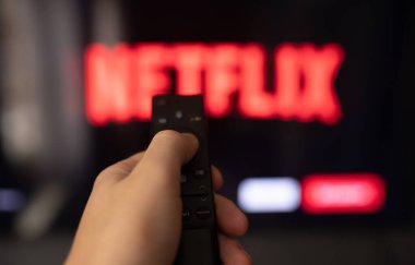 Adamın elinde arka planda televizyon ekranı olan akıllı bir televizyonun uzaktan kumandası var. 