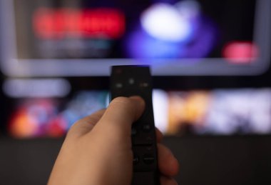 Adamın elinde arka planda televizyon ekranı olan akıllı bir televizyonun uzaktan kumandası var. 