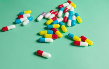 Yeşil arkaplandaki renkli tıbbi kapsüllerin yakın plan görüntüsü.   