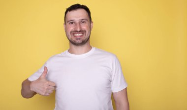 Sarı arka planda baş parmak gösteren genç adam portresi. 