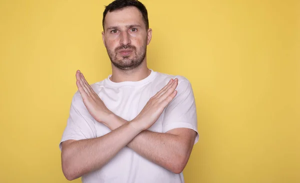 stock image portrait of young man in white shirt gesturing no on yellow background   