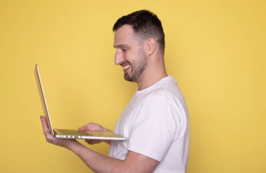 Dizüstü bilgisayarı olan mutlu genç adam sarı arkaplanda kopya alanı ile izole edilmiş.