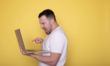 duygusal genç adam sarı arka planda dizüstü bilgisayar kullanıyor..