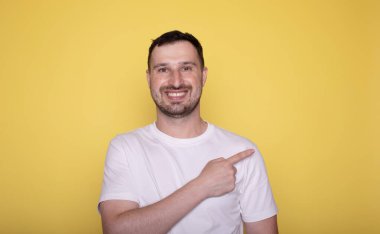 Sıradan tişörtlü genç adam sarı arka planda izole edilmiş bir şey sunuyor..