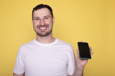 Mutlu adam akıllı telefonunda boş ekran gösteriyor, sarı arka planda izole edilmiş.      