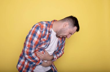 Karın ağrısı çeken genç yakışıklı bir adam, sarı arka planda izole edilmiş.