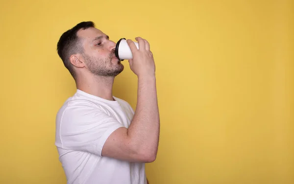 stock image handsome young man drinking coffee from paper cup on yellow background