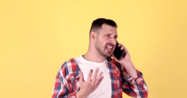 Sarı arka planda izole edilmiş akıllı telefondan konuşan sinirli genç sakallı adam.