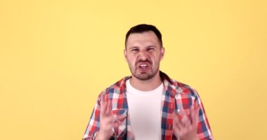 Sinirli genç sakallı adam sarı arka planda izole edilmiş kameraya bağırıyor.
