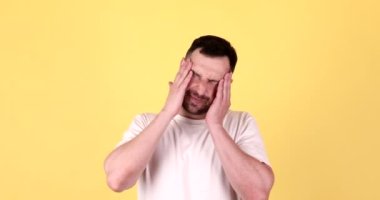 Mutsuz üzgün bir adam şakaklarına masaj yapıyor, sarı arka planda stüdyoda korkunç bir acıyı dindirmeye çalışıyor..