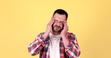 Mutsuz üzgün bir adam şakaklarına masaj yapıyor, sarı arka planda stüdyoda korkunç bir acıyı dindirmeye çalışıyor..