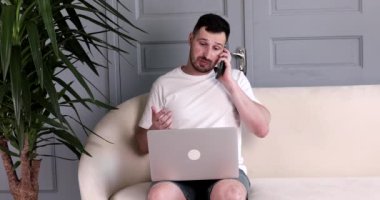 Sakallı yakışıklı genç adam kanepede oturuyor ve evde dizüstü bilgisayar kullanıyor..