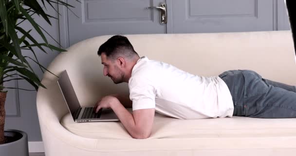 Bebaarde Knappe Jonge Man Liggend Bank Met Behulp Van Laptop — Stockvideo
