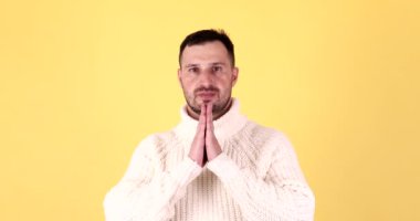 El ele tutuşup düşünceli yoga yapan, sakinleşmeye çalışan meditasyon yapan ve sarı arka plana konsantre olmaya çalışan genç bir adam..