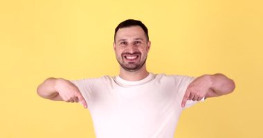 Temel kameradaki genç adam sarı arka plan stüdyosunda izole edilmiş fotokopi alanı çalışma alanını işaret ediyor. Halk yaşam tarzı konsepti.