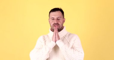 Sakallı adamın portresi, dua ediyor, yalvarıyor, el ele tutuşuyor, umut dolu bir yüz ifadesiyle sarı arka planda izole edilmiş..