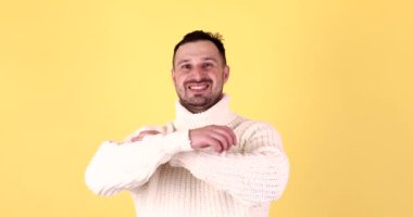 Yakışıklı sakallı genç adam kollarını kavuşturmuş ve sarı arka planda izole edilmiş kameraya gülümsüyor.