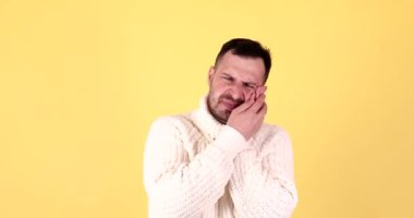 Sarı arka planda diş ağrısından muzdarip yanağa dokunan genç bir adam..