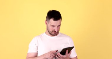 Sarı arka planda izole edilmiş dijital tablet kullanan yakışıklı sakallı genç adam.