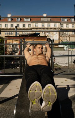 Atletik adam şehir parkının açık hava spor salonunda egzersiz yapıyor.