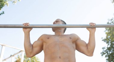 Kaslı sporcu açık havada barfiks çekiyor. Spor eğitmeni sokak antrenmanında. Formda ve atletik bir adam