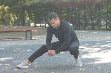 Yakışıklı genç sporcu dışarıda esneme egzersizleri yapıyor.  