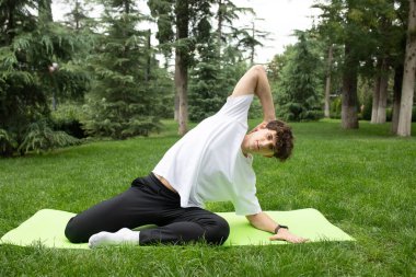 Güneşli bir sabahta parkta yoga yapan bir adam. Açık havada yoga minderinde egzersiz yapan sağlıklı ve aktif yaşam tarzı kavramı olan zinde bir genç. Açık havada eğitim..